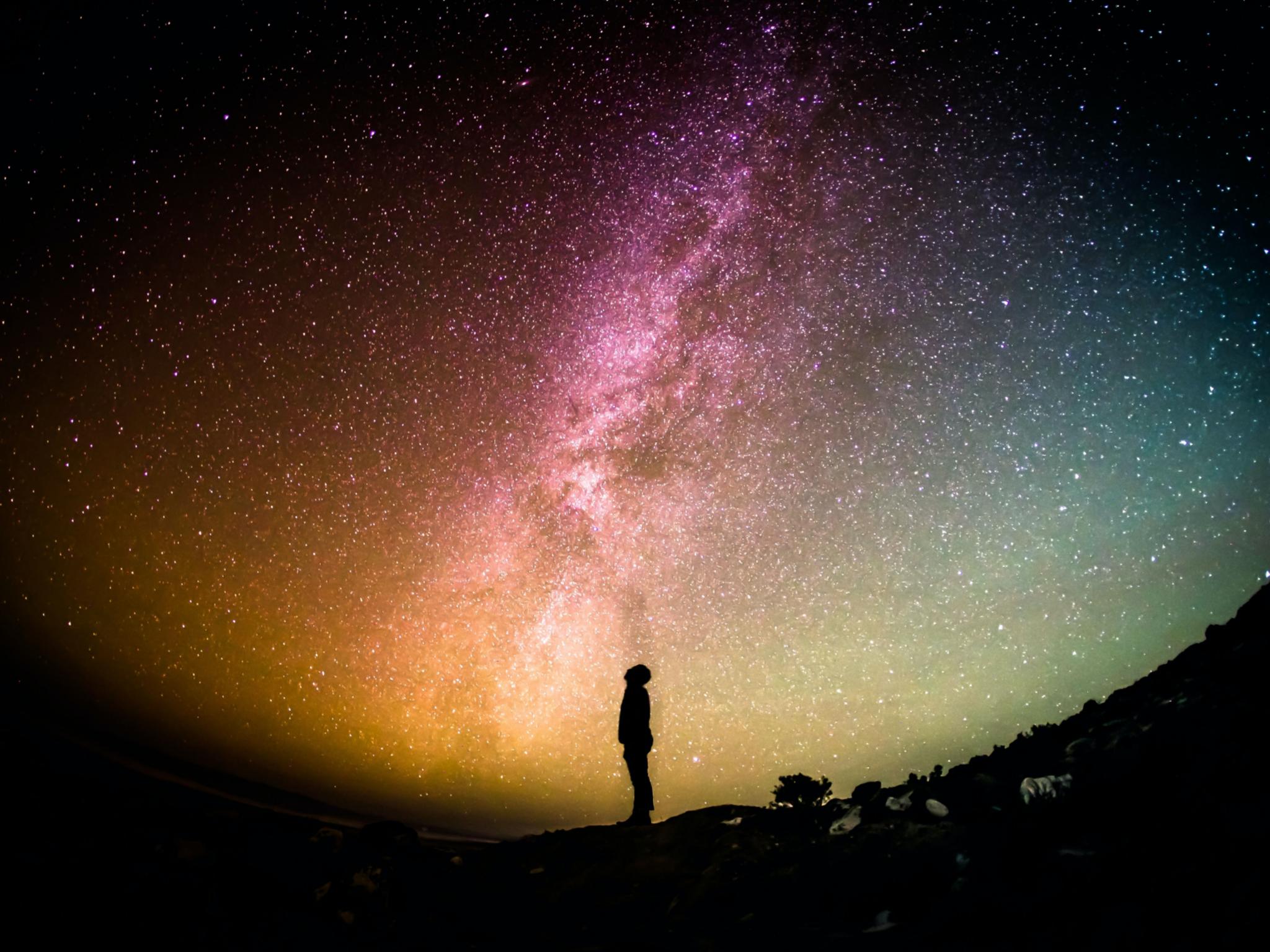 Ein Mensch steht vor einem Sternenhimmel. Man sieht die Milchstraße
